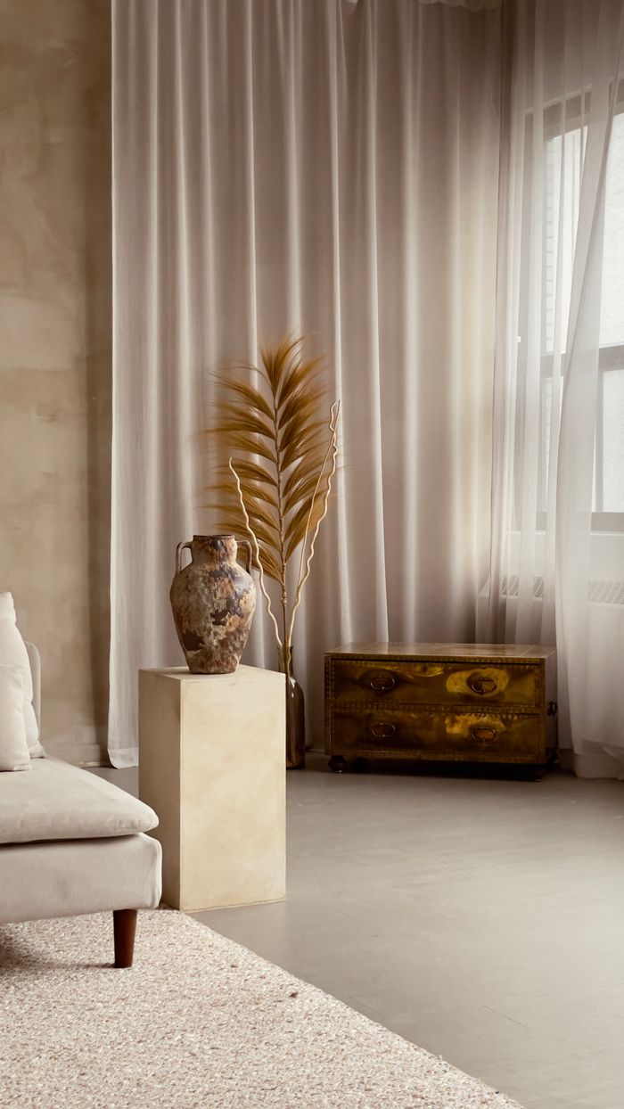 Elegant wabi sabi styled room with neutral decor featuring a metal vase and tall curtains in soft lighting.