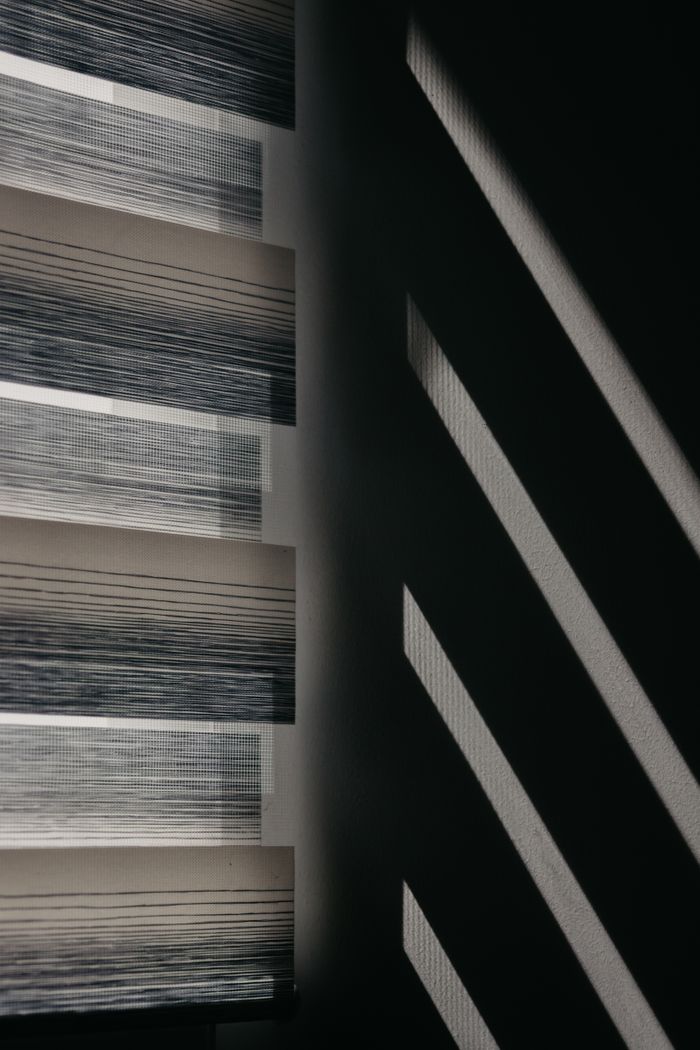 Modern window blinds create striking shadows on a wall for an abstract visual effect.